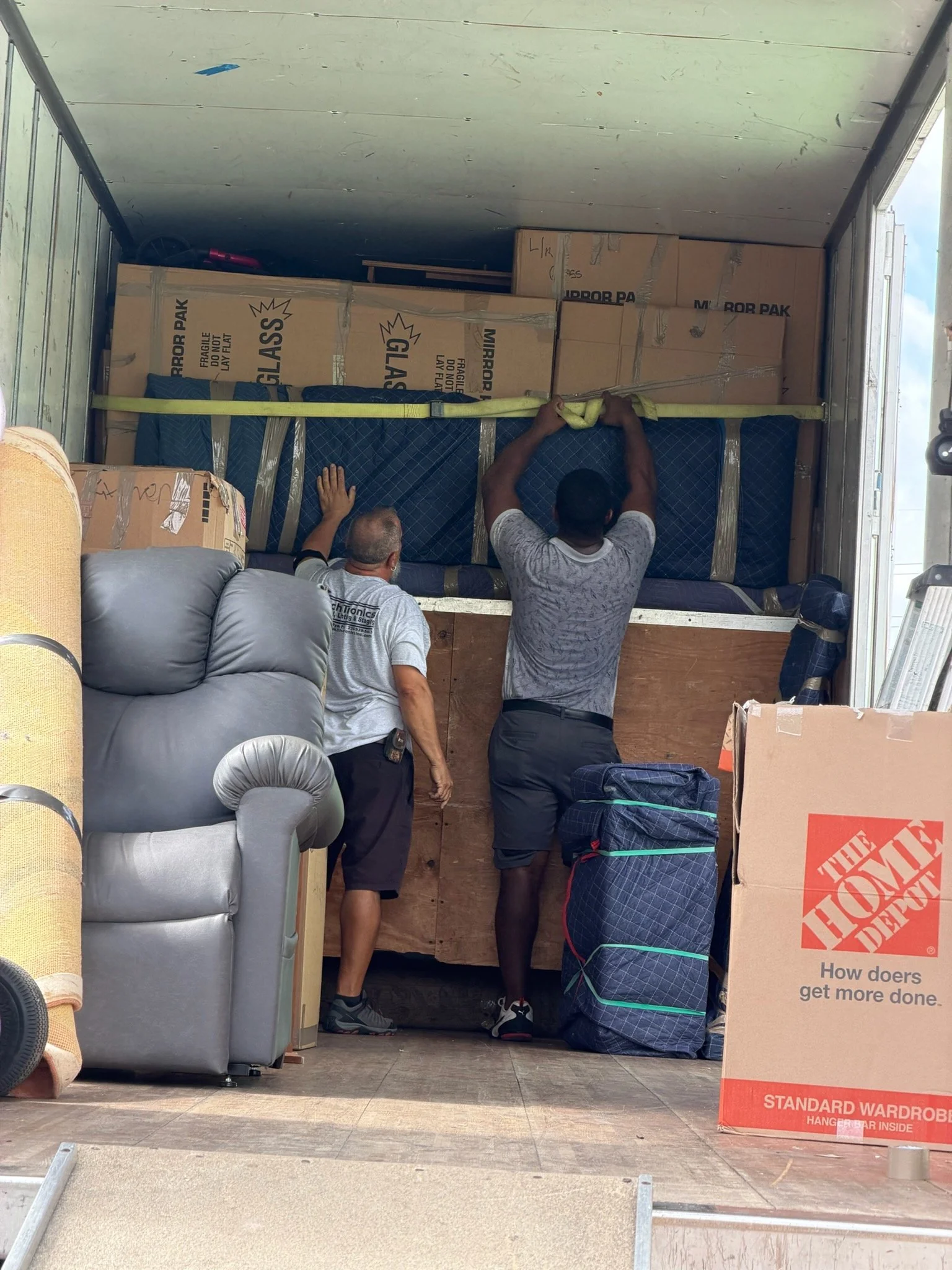 Two movers securing padded furniture and cartons inside a moving truck