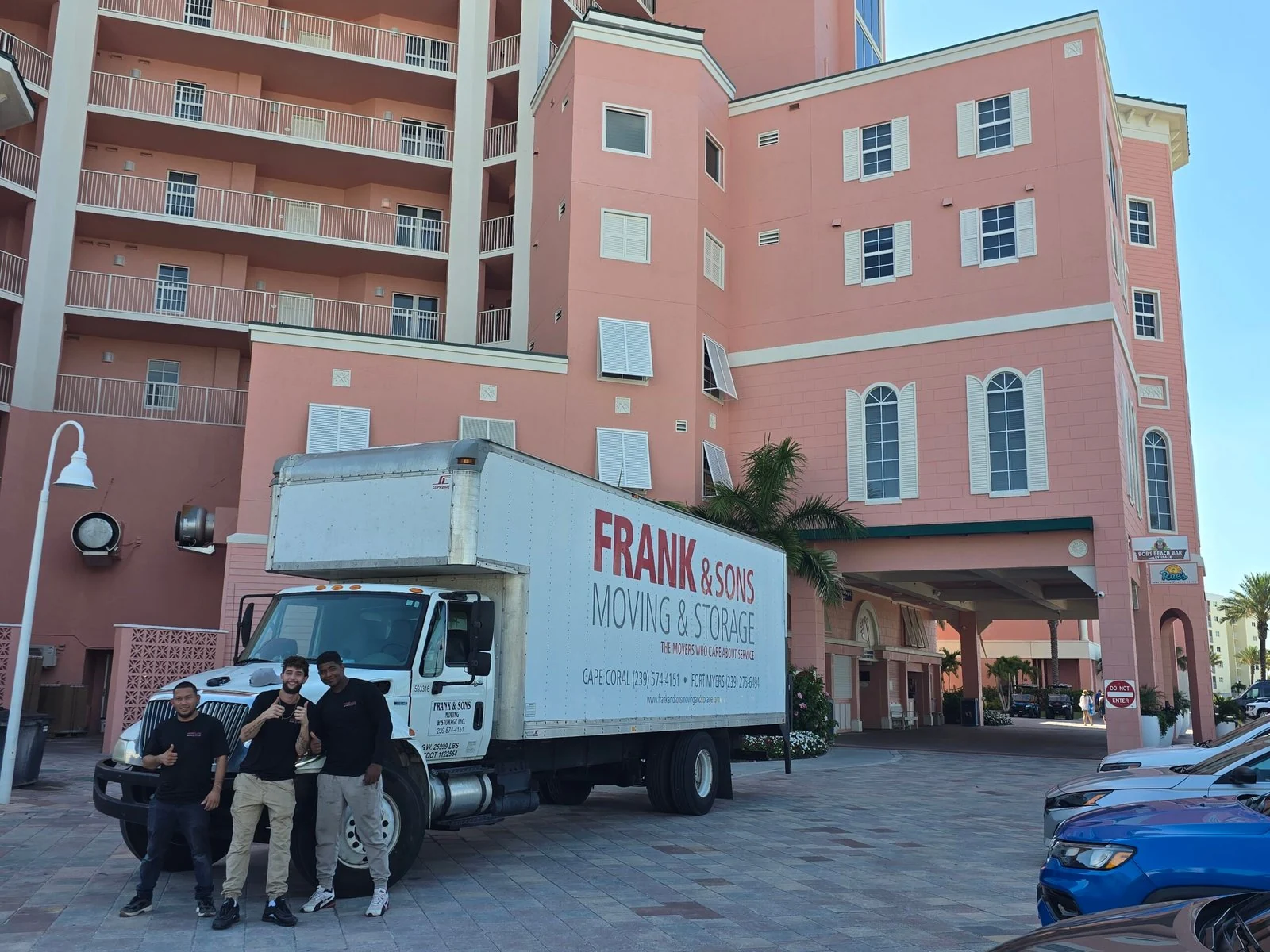 Three Frank and Sons crew members beside a moving truck outside a pink condominium