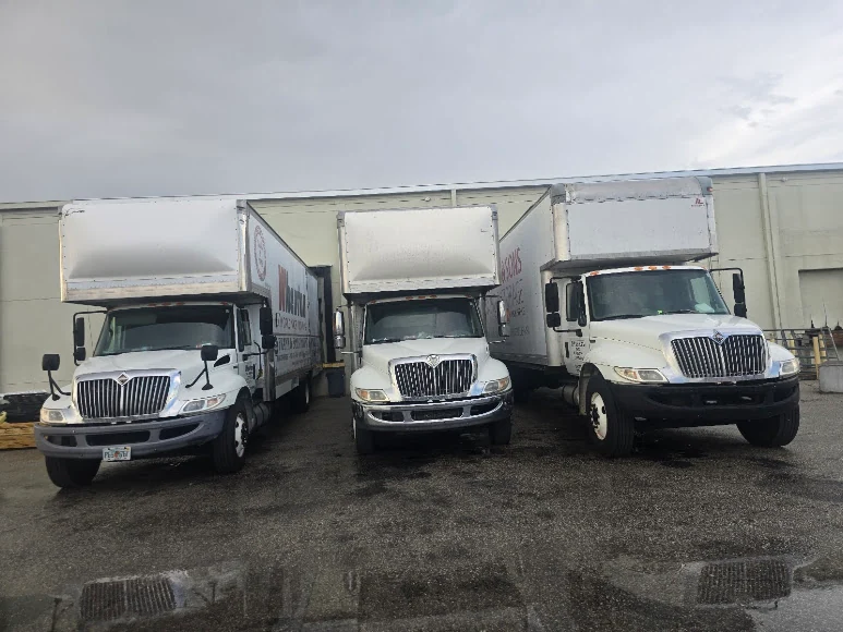 Three Frank and Sons moving trucks parked outside a warehouse