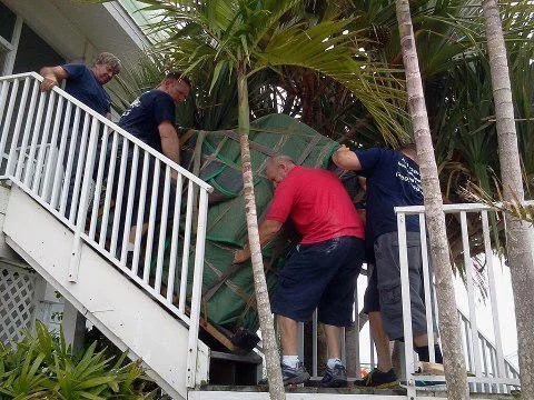 Moving crew carefully carrying a padded furniture piece along an outdoor staircase