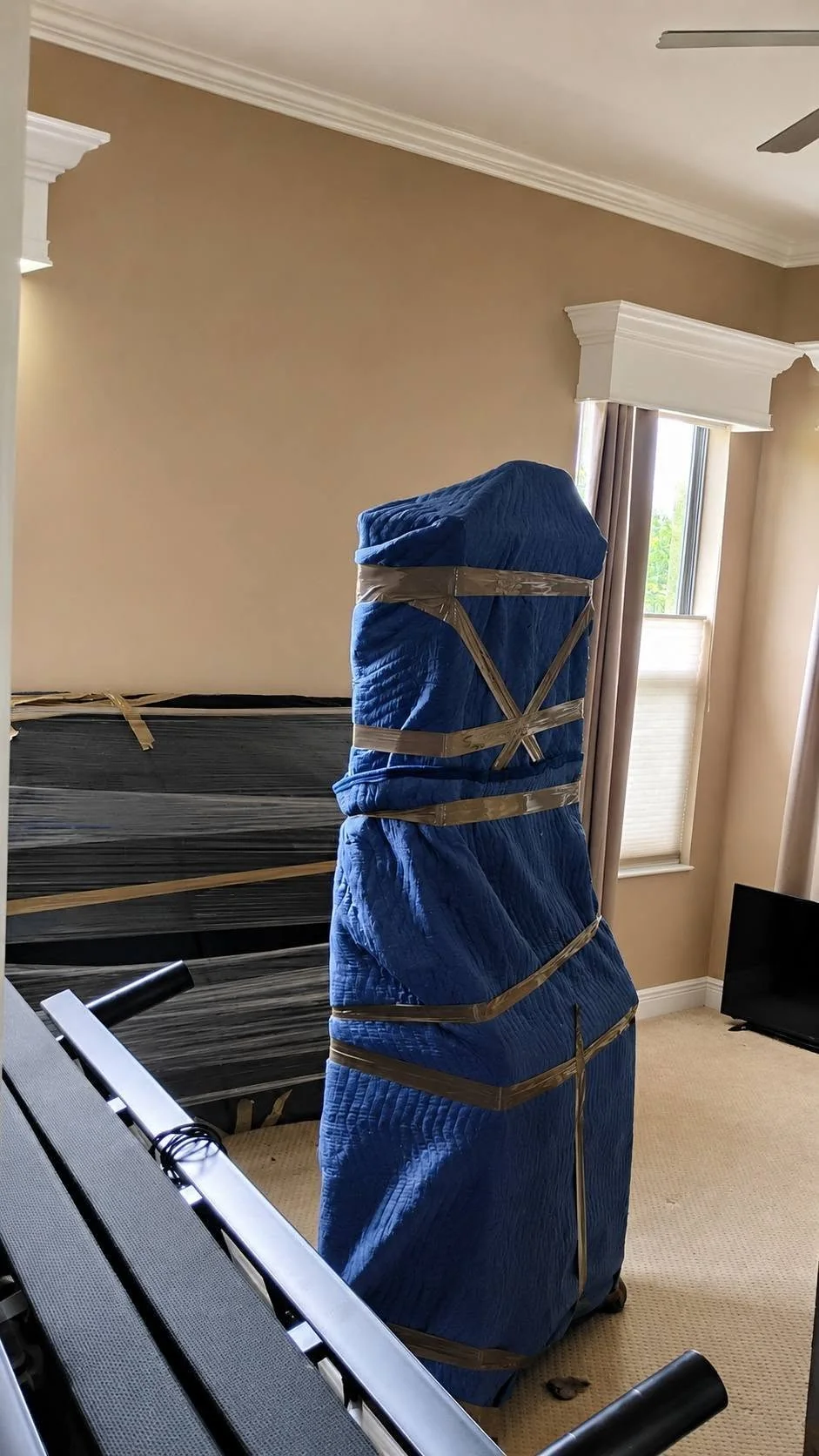 A tall furniture piece wrapped in blue moving blankets inside a home
