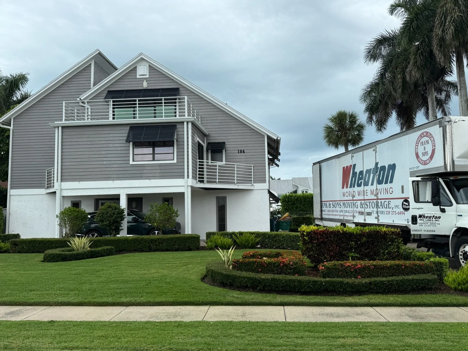 A branded moving truck parked beside a gray coastal style home