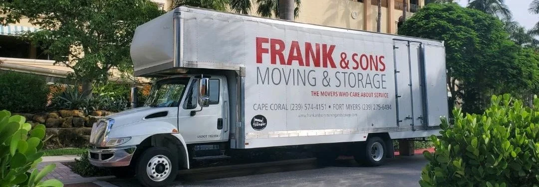 A Frank and Sons moving truck beside trees and garden planting