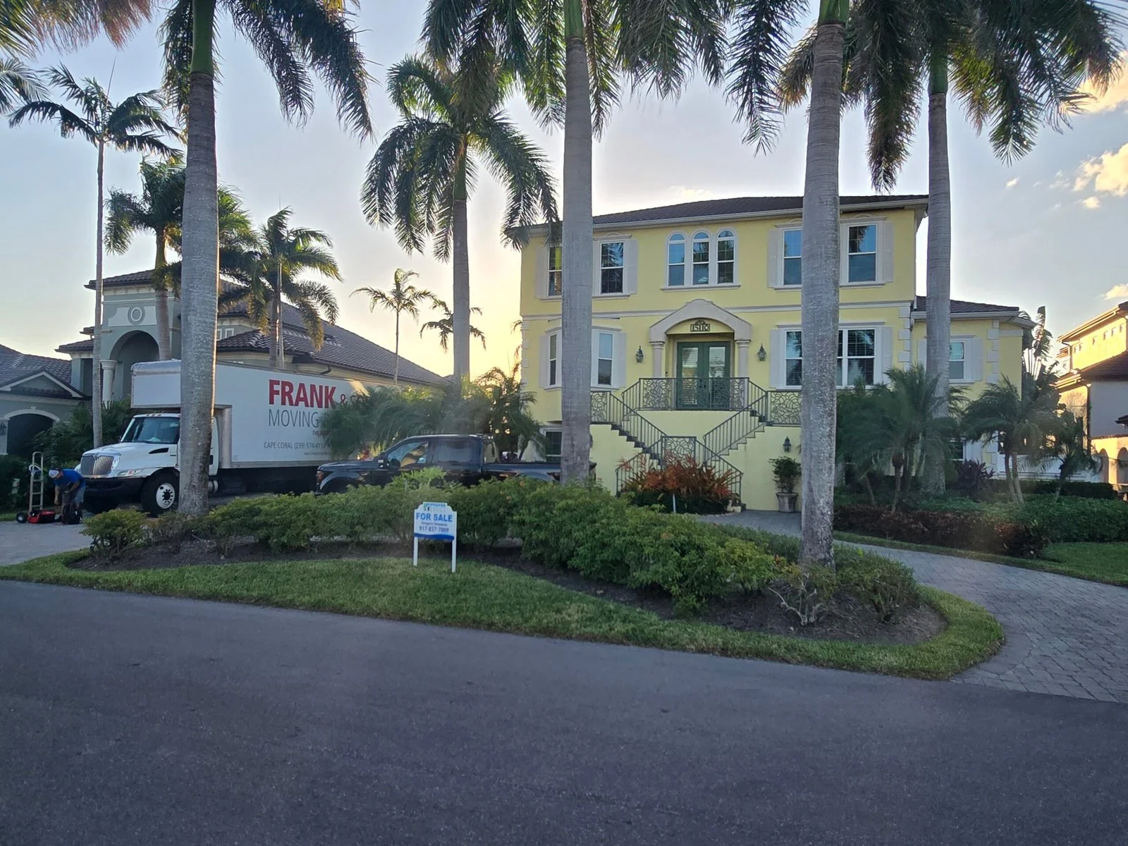 Frank and Sons moving truck beside a yellow coastal home and palms